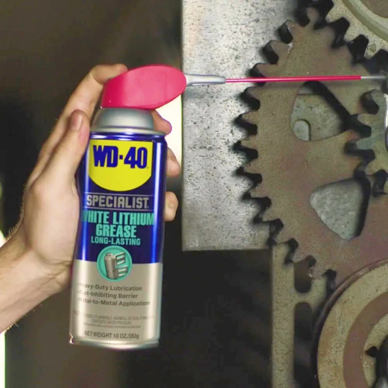 Hand holding WD40 Specialist Spray White Lithium Grease Lubricant can near metal gears.