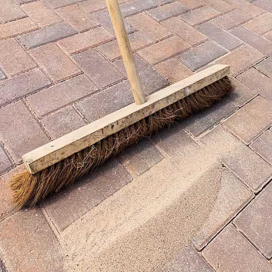 Broom brushing sand into joints of brick paving during application of Joint-It Fine