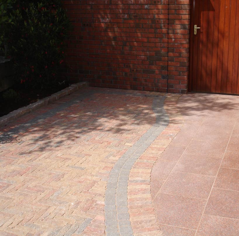 Brick driveway with a curved path leading to an entrance, showing paving joints filled with sand