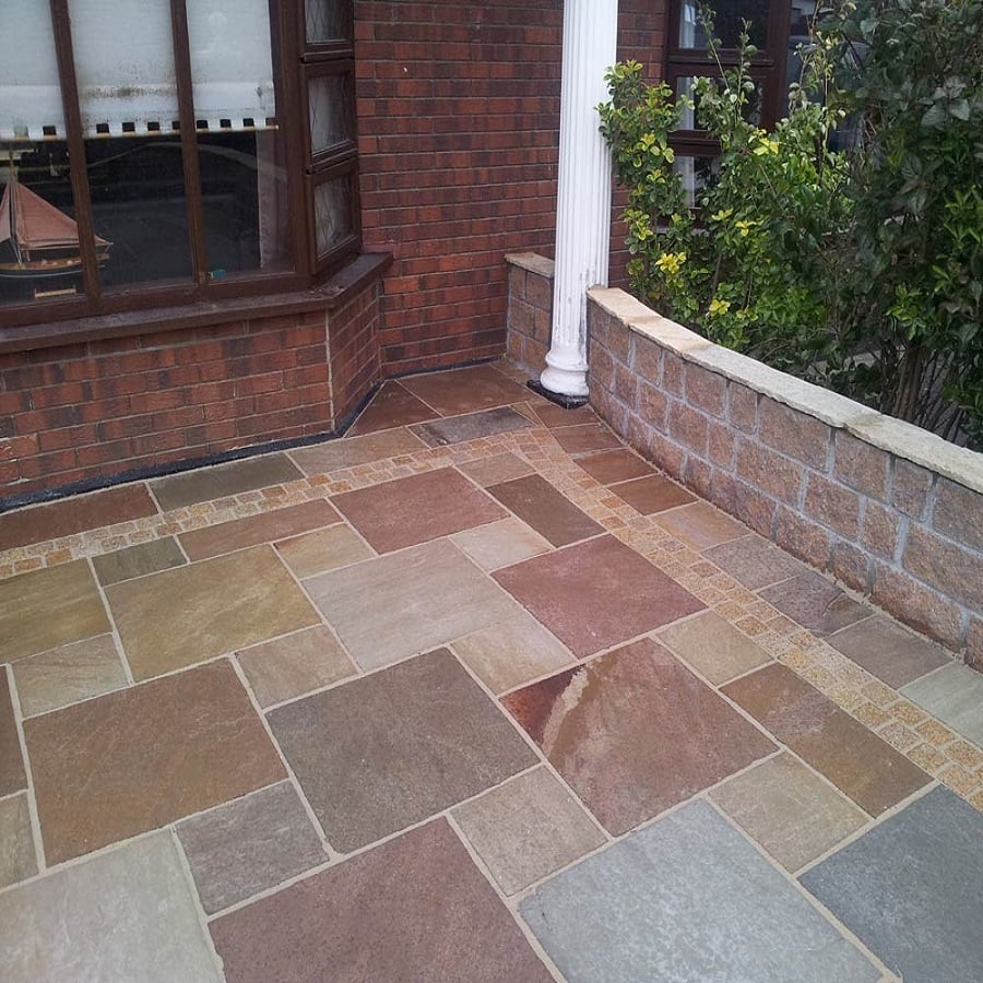 Patio laid with coloured sandstone tiles and brick edging