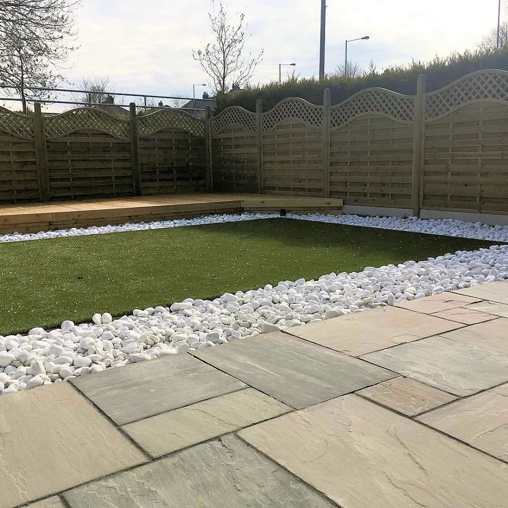 Artificial lawn surrounded by grey sandstone paving and white decorative stones