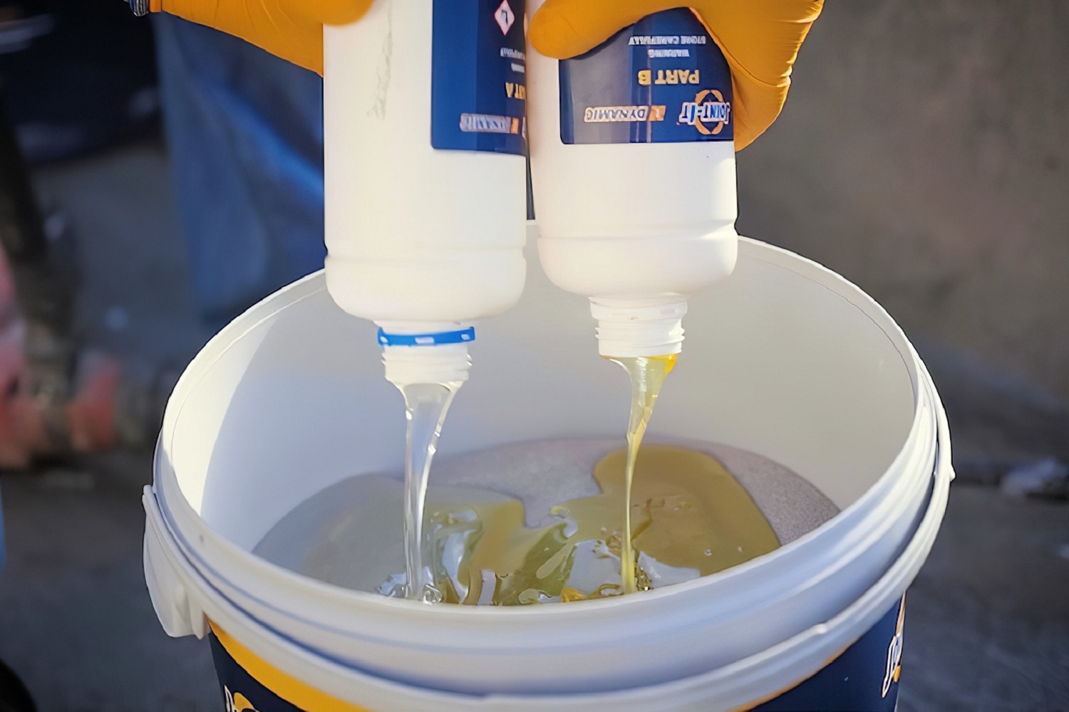 Two resin components being poured into a bucket for mixing before joint application