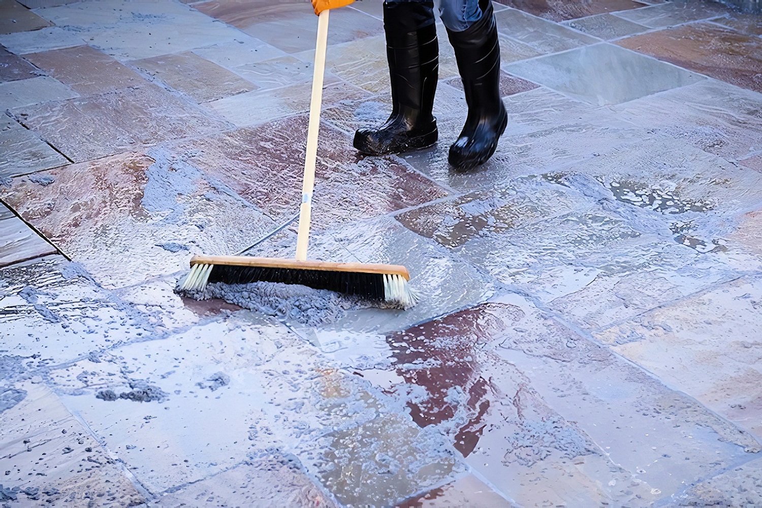 Person brushing resin jointing mix into wet stone paving joints during application