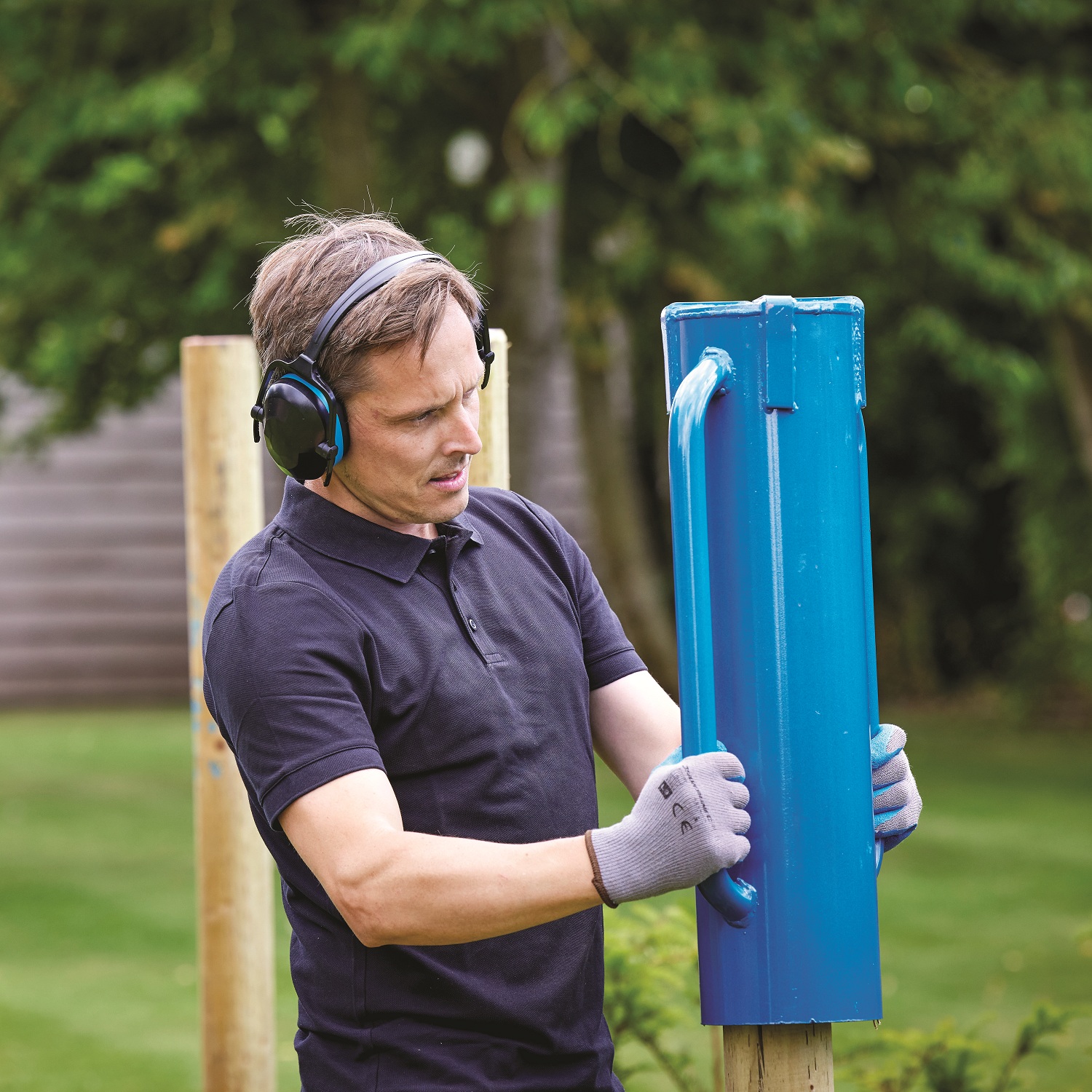 Blue steel rammer tube driver with handles next to a wooden fence post in use