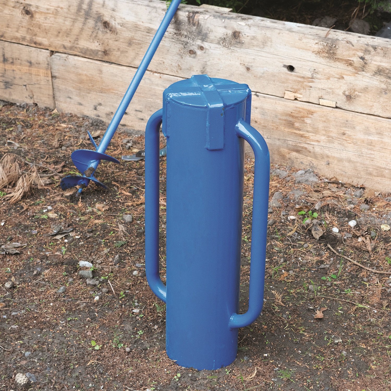 Blue steel rammer tube driver with handles next to a wooden fence post demo with auger