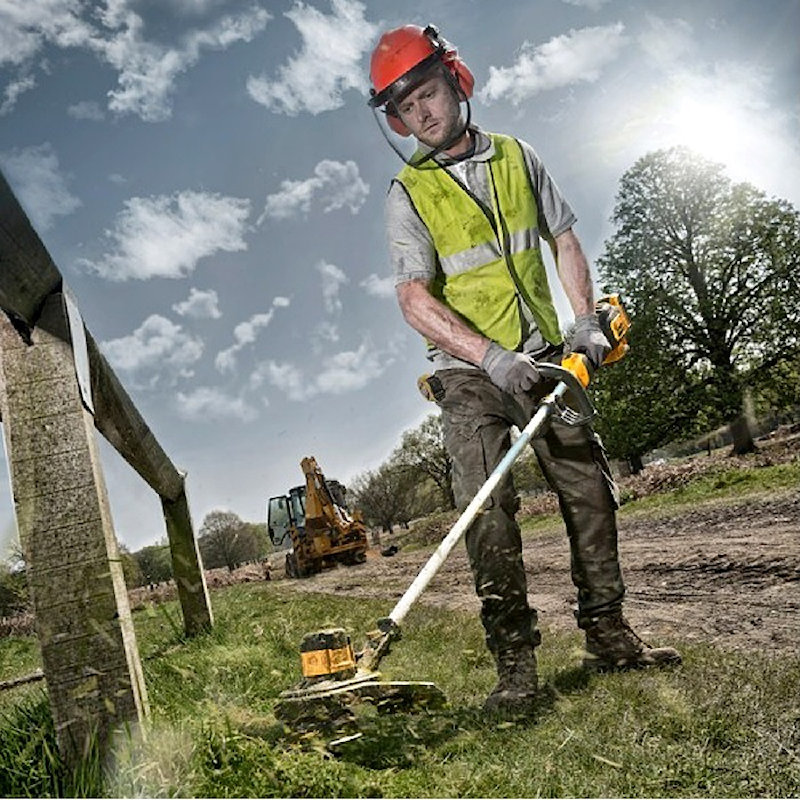 Person using a DeWalt cordless brushless 18v grass strimmer in a field