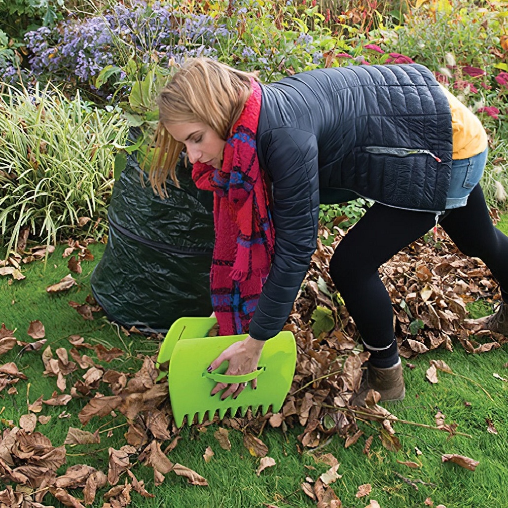 Person using green leaf collector scoops to gather fallen leaves from the lawn