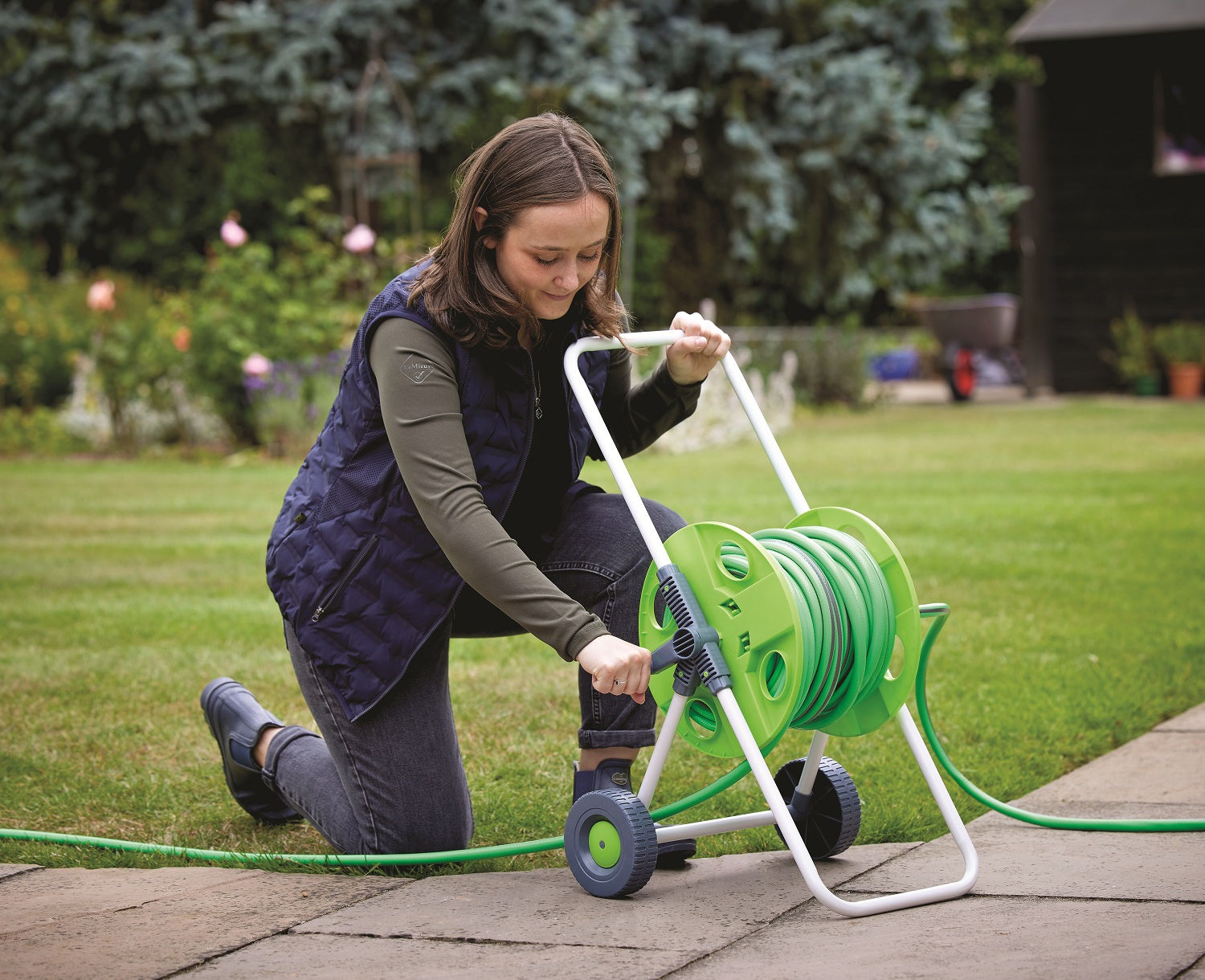 Green and silver wheeled standing hose pipe reel with handle and wheels for easy movement in use in garden