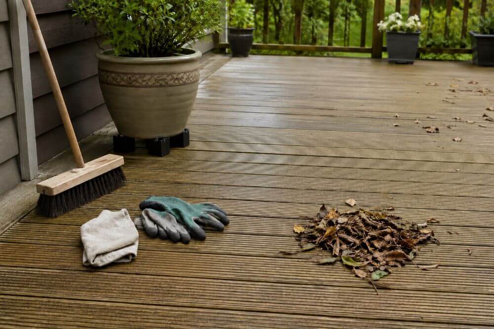 Regular timber decking maintenance with broom and cleared leaves