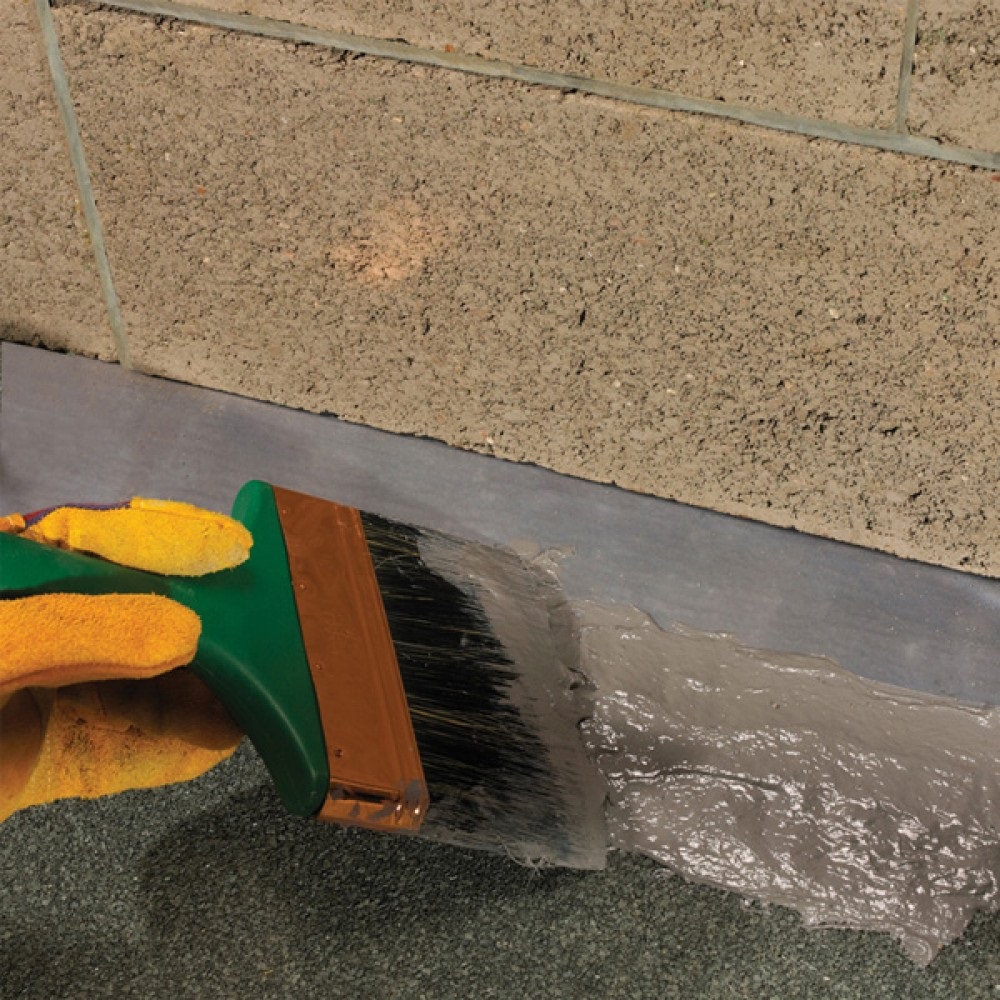 Grey Sika Evercryl roof repair compound brush applied along wall flashing on a flat roof