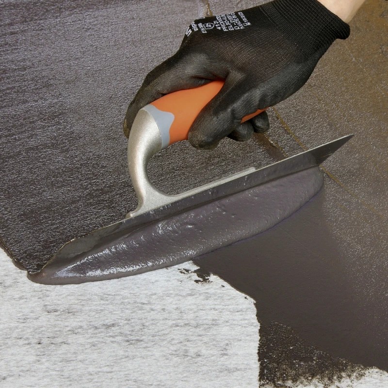 Applying Sika Black Jack 903 Bitumen Trowel Mastic with a trowel during a roof waterproofing repair on roofing felt and bitumen surfaces