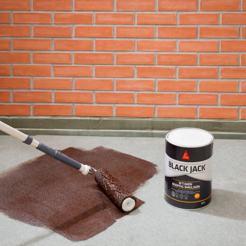Sika Black Jack 906 Bitumen Roofing Emulsion being applied with a roller to a roof surface near brickwork