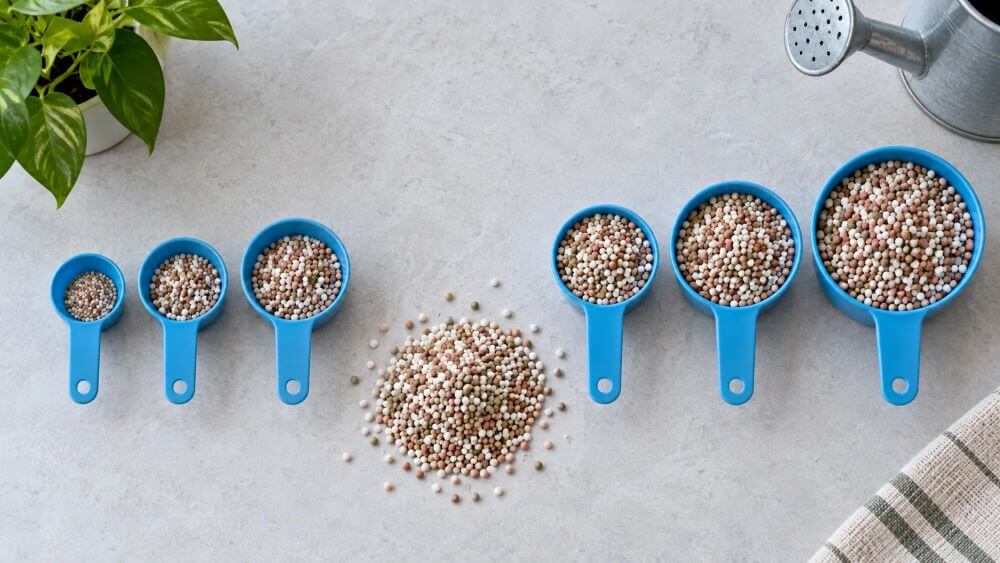 Measuring cups show different quantities of fertiliser granules in matching proportions.