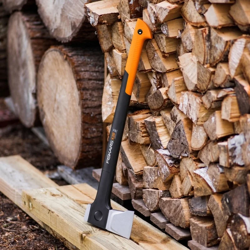 Fiskars splitting axe leaning against a stack of cut firewood with its orange handle end raised.