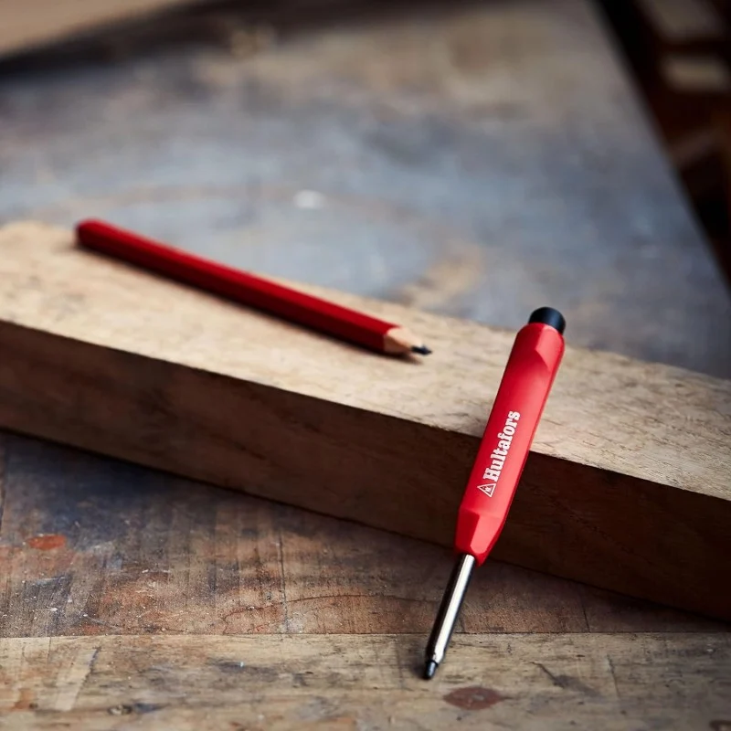 Red Hultafors dry marker resting against timber on a workbench, with a pencil lying behind it.